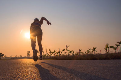 Rear view of woman running on road against sky during sunset