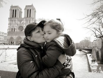 Mother kissing daughter in city during winter