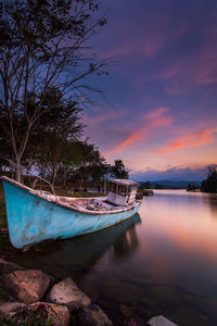 Boat moored in lake against sky at sunset