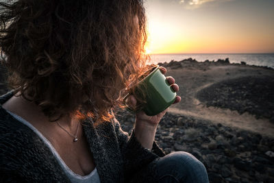 Close-up of woman drinking coffee against sunset