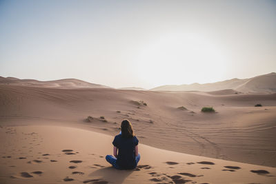 Rear view of woman sitting on desert against sky