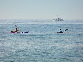 Men canoeing in sea against sky