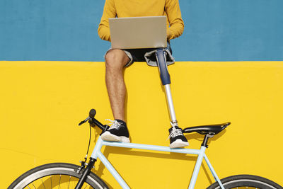 Man with artificial limb and foot using laptop while sitting on multi colored wall