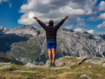 Rear view of woman with arms raised looking at mountains against sky