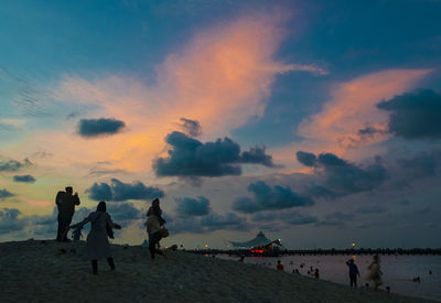 People walking on beach against sky during sunset