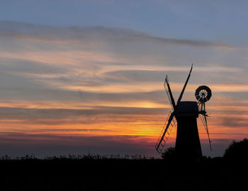 Silhouette of windmill on field against sky during sunset