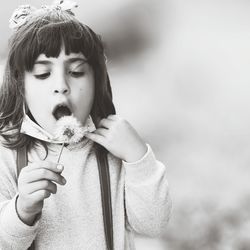 Portrait of cute girl holding dandelion against white background