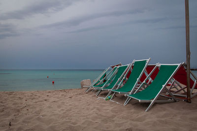 Deck chairs on beach against sky