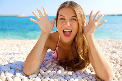 Portrait of smiling young woman lying on pebbles at beach