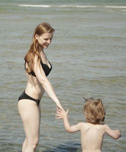 Woman in bikini holding son hand at sea shore