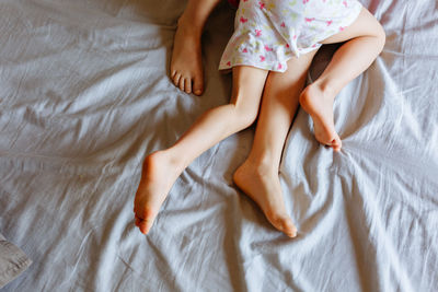 Legs of two children lying and playing on the grey bed