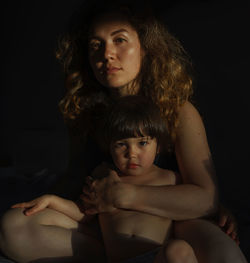 Portrait of woman with baby sitting against black background