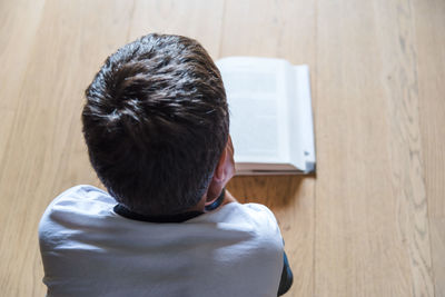Rear view of boy reading book while sitting on floor