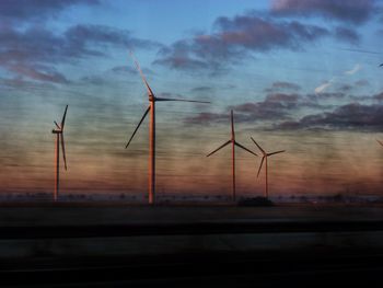 Silhouette windmills against sky at sunset