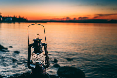 Close-up of lantern by lake against sky during sunset