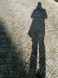 High angle view of shadow of person standing on cobblestone