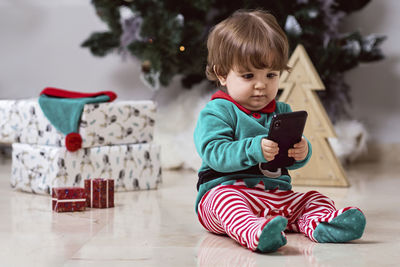 A little 12-month-old christmas elf with a christmas tree and gifts