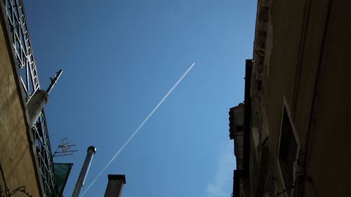 Low angle view of vapor trails against clear blue sky