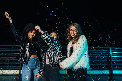 Smiling young women enjoying while standing outdoors at night