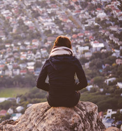 Rear view of woman sitting on rock against cityscape