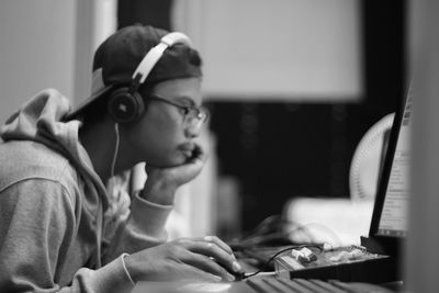 Side view of young man wearing headphones while using computer at desk