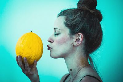 Profile view of woman kissing cantaloupe against turquoise background