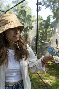 Beautiful young woman feeding a bird with a wooden stick with seeds stuck to it, bird