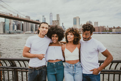 Portrait of happy friends standing against railing in city