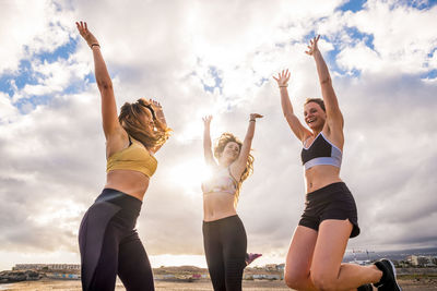 Low angle view of friends jumping against cloudy sky at beach