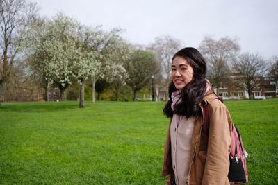 Happy young woman standing on grass against trees