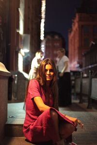 Portrait of young woman smoking while sitting outdoors at night