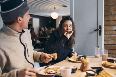 Woman eating breakfast while sitting with friend at table in log cabin