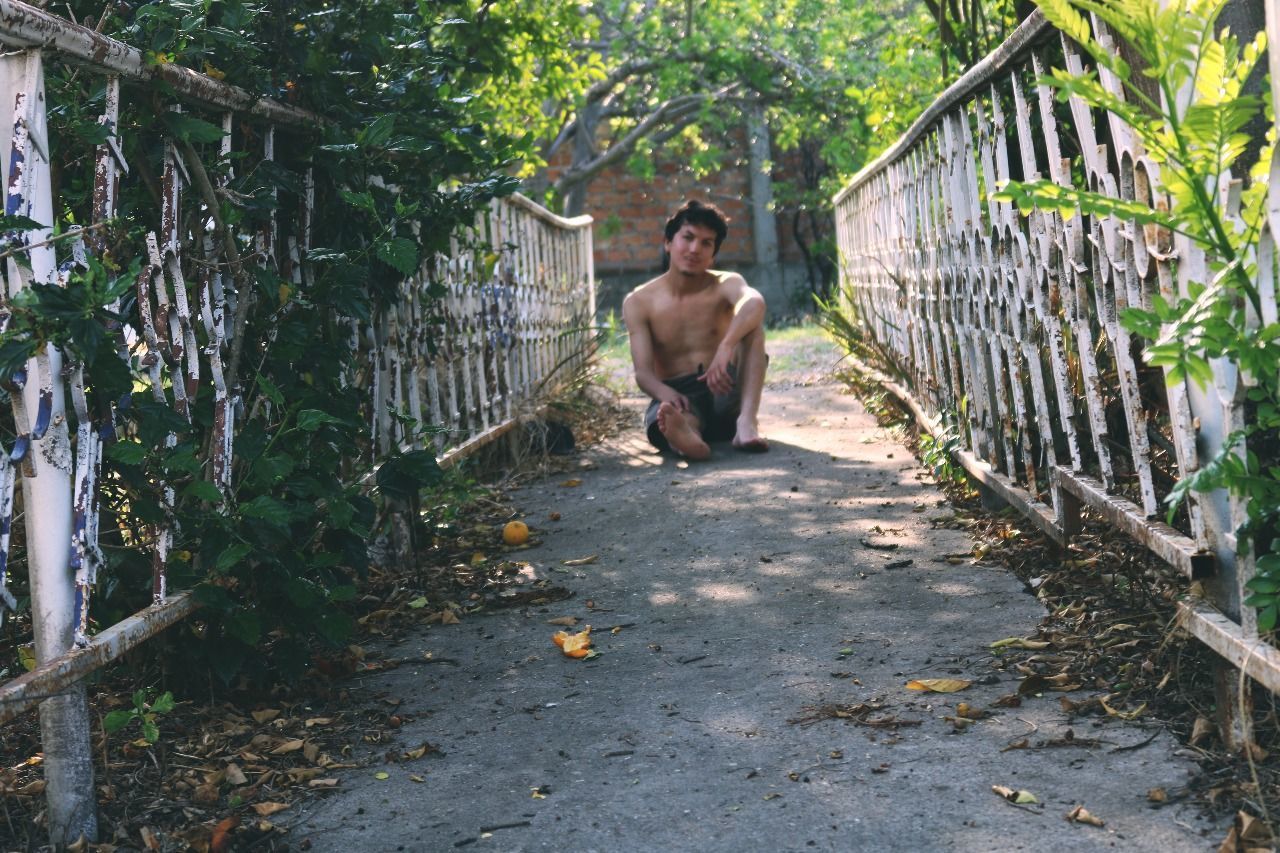 FULL LENGTH OF SHIRTLESS YOUNG MAN STANDING ON TREE