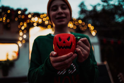 Portrait of boy holding jack o lantern cup at home