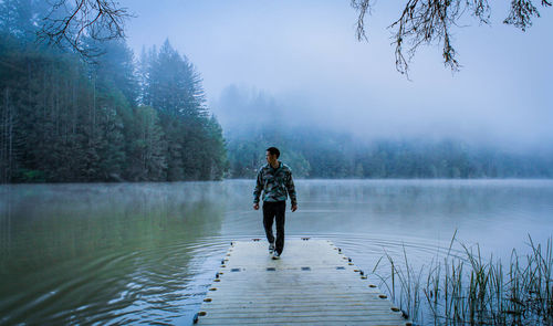 Rear view of woman on lake in forest during foggy weather