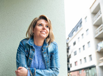 Optimistic woman in blue denim jacket glancing skyward with a smile