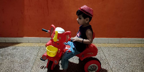 Cute boy riding toy car against wall