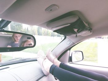 Low section of woman with friend on back seat reflecting in car rear-view mirror