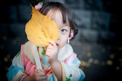 Portrait of cute girl covering face with leaf