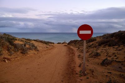 Road sign by sea against sky