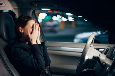 Happy woman covering face with hands sitting in car