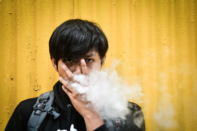 Portrait of young man smoking cigarette against wall