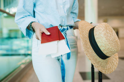 Midsection of woman holding passport and hat