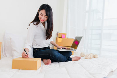 Young woman using phone while sitting on bed