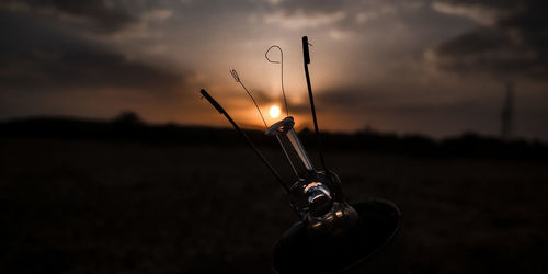 Close-up of silhouette metal on field against sky at sunset