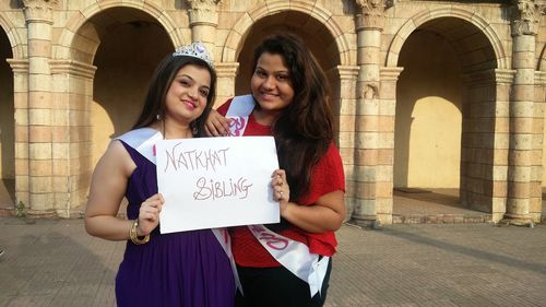 Portrait of smiling females showing placard while standing against building