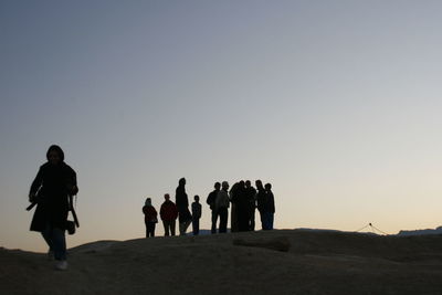 People walking on desert against clear sky during sunset