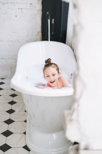 Happy little girl having fun in bath with foam at home