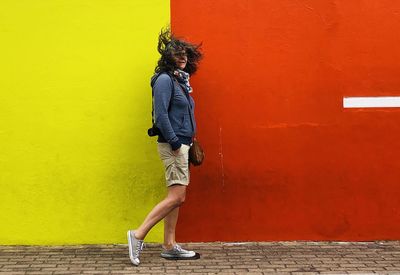 Full length of woman with tangled hair walking ob sidewalk against colored wall