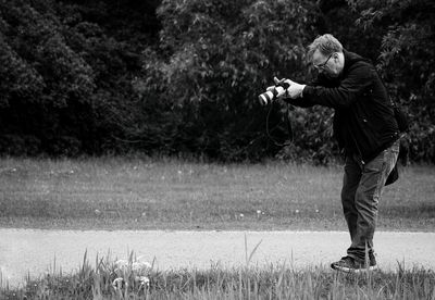 Side view of man photographing while standing on field at park